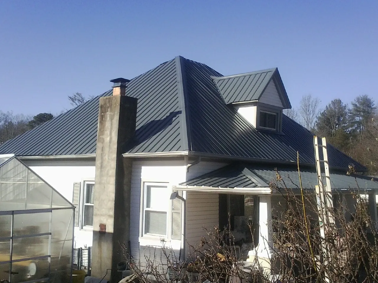 Dark blue standing seam metal roof on a white farmhouse with dormer — Slate & Tile Roof Repair by Roofing Brothers in Sealy