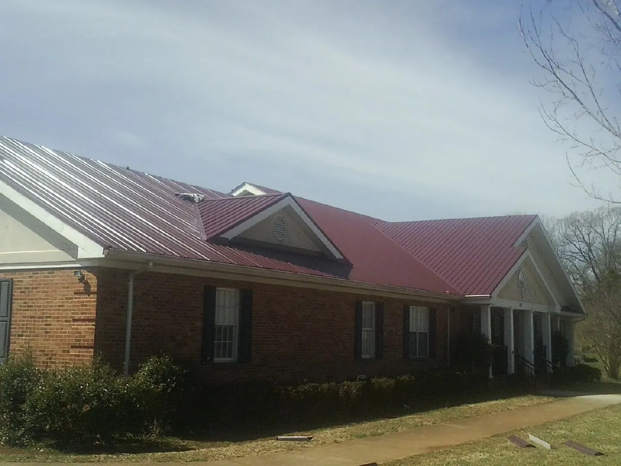 Red metal roof with gabled entries on a long brick building, from a Hail Damage Roof Repair job in Sealy