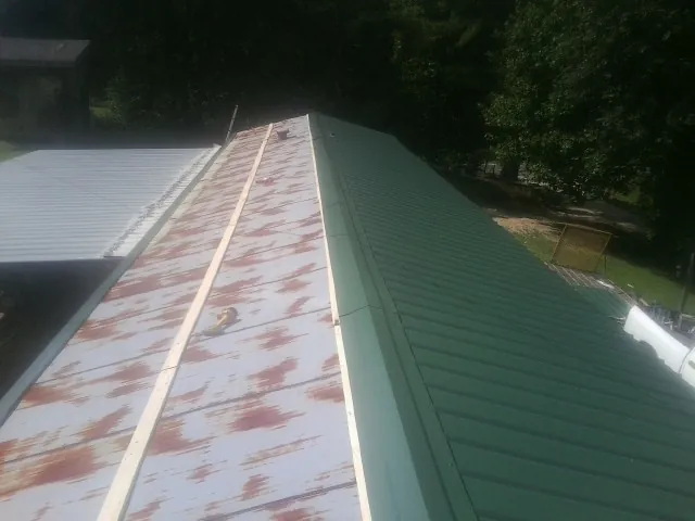 Old rusted panels beside newly installed green metal roofing — Wind Damage Roof Repair by Roofing Brothers in Sealy