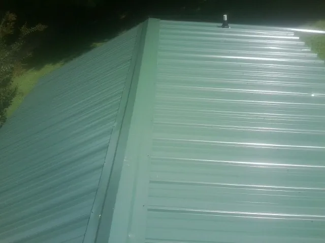New green metal panels meeting at the ridge of a roof — Flat Roof Repair work by our crew in Sealy