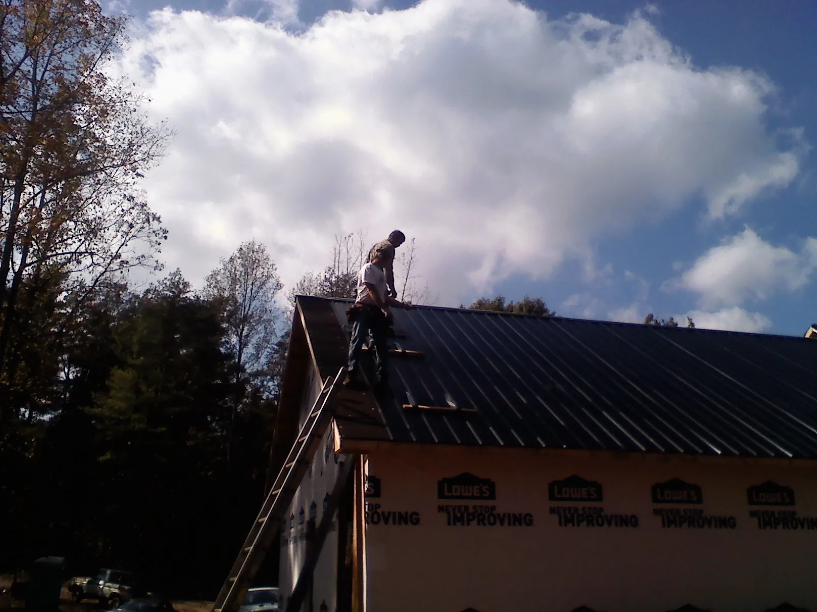 Roofer fastening dark metal panels high against a cloudy sky, from a Roof Inspection job in Sealy
