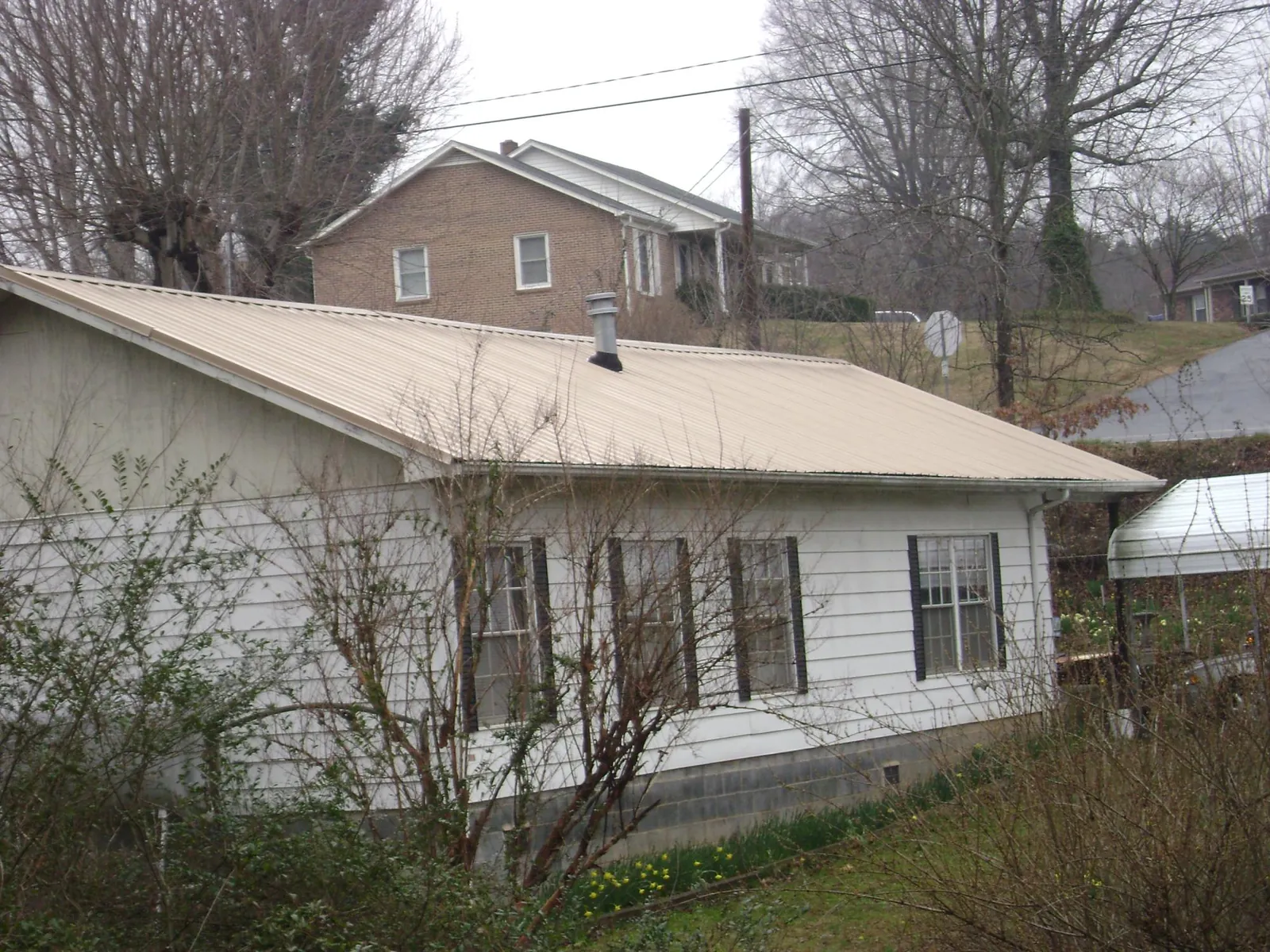 Tan metal roof on a white sided house set into a hillside — Commercial Roofing by Roofing Brothers in Sealy